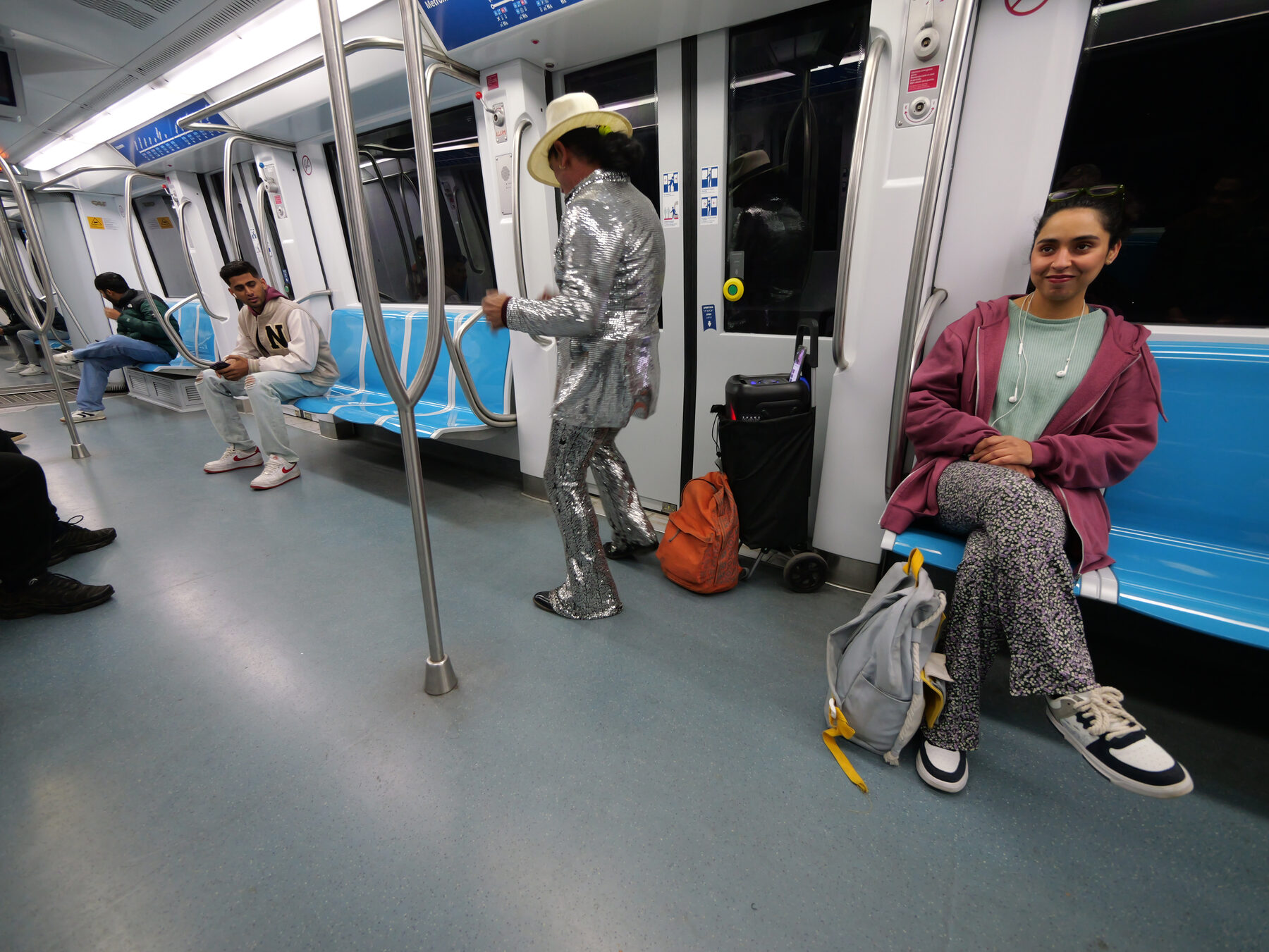 Metro performer in a sequined silver suit walks the aisle as a seated passenger looks on
