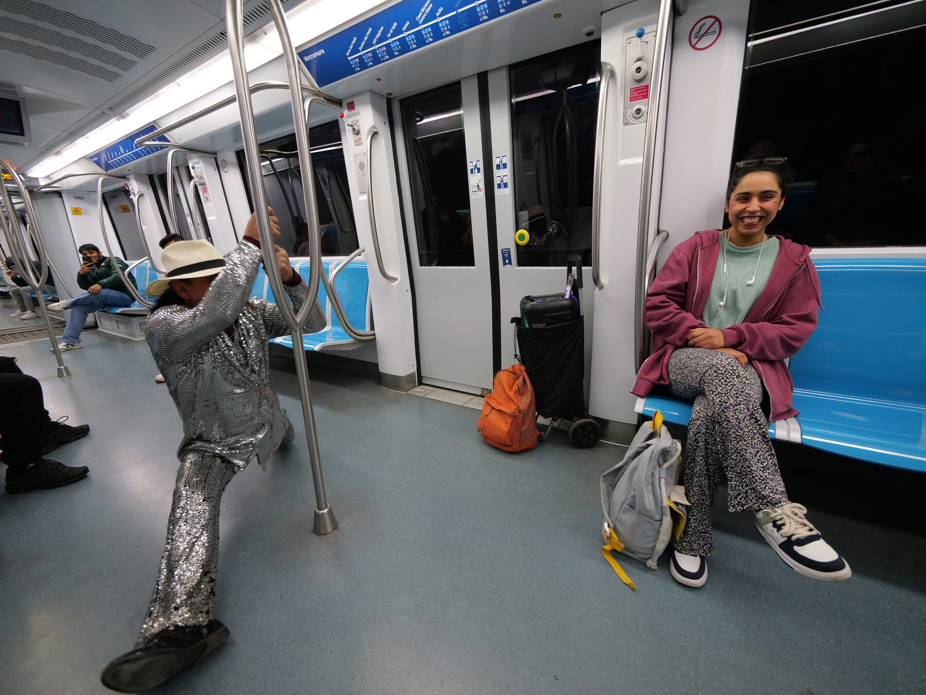 The performer swings from a pole, the passenger grinning across the car